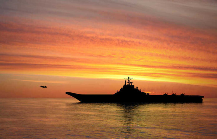 Silhouette of an aircraft carrier at sunset.