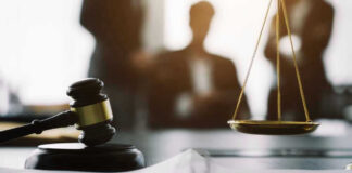 Gavel and scales in courtroom with blurred figures behind.