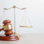 A wooden gavel in front of a balance scale symbolizing justice