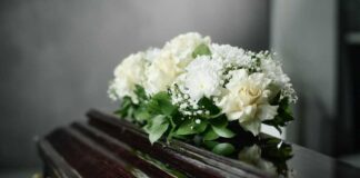 A floral arrangement of white roses and greenery on a polished casket