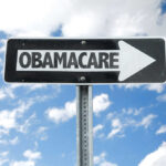 Directional sign pointing towards Obamacare against a blue sky