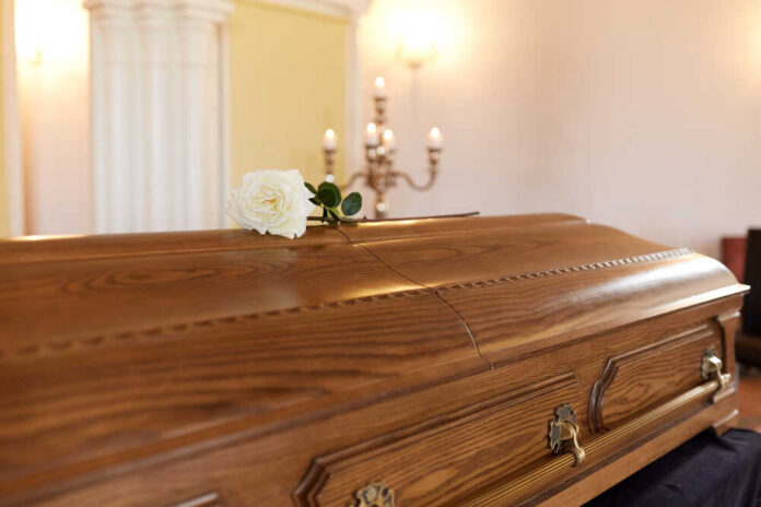 shutterstock_678983125.jpg A wooden casket with a white rose placed on top in a solemn setting