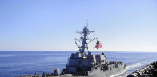 Warship with American flag sailing in the ocean.