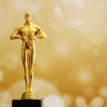 Golden Oscar trophy against a sparkling gold background.