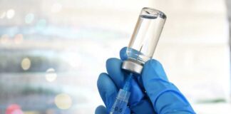 A gloved hand holding a syringe and a vial of liquid