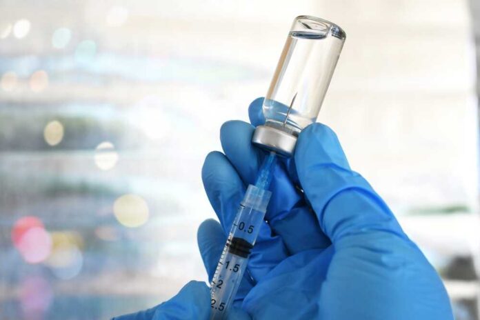 shutterstock_2288390279.jpg A gloved hand holding a syringe and a vial of liquid