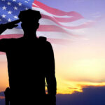 Silhouette of soldier saluting in front of flag
