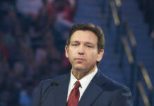 DeSantis Puts Trump Name on Airport Man in suit speaking at a public event.