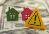 Colorful house models and a warning sign on dollar bills