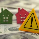 Colorful house models and a warning sign on dollar bills