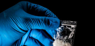 Hand in glove holding bag of white powder.