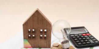 A wooden house model, light bulb, coins, and a calculator on financial documents