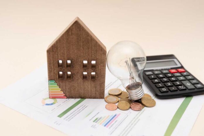 A wooden house model, light bulb, coins, and a calculator on financial documents