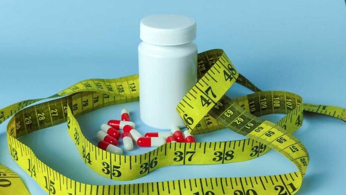 A white pill bottle surrounded by red and white capsules and a yellow measuring tape