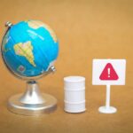 War DESTROYS More Oil Than Entire Pandemic A miniature globe next to a warning sign and a barrel