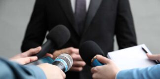 Journalists holding microphones and a notepad during a press conference