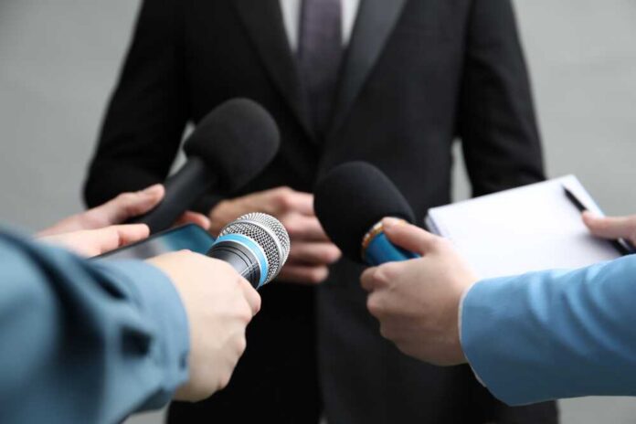 shutterstock_2566792697.jpg Journalists holding microphones and a notepad during a press conference