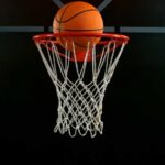 A basketball is about to enter a hoop against a dark background