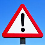 Driver Plows Through Crowd – Mass Casualty Event A triangular warning sign with an exclamation mark against a blue sky