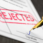 A rejection notice with a red stamp and a pen about to sign