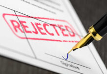 A rejection notice with a red stamp and a pen about to sign