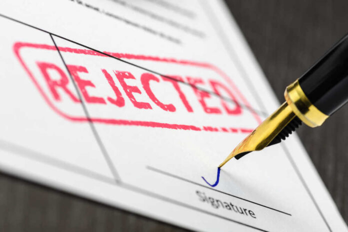 A rejection notice with a red stamp and a pen about to sign