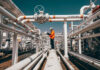 Worker in orange jacket inspecting industrial pipes.