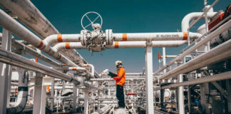 Worker in orange jacket inspecting industrial pipes.
