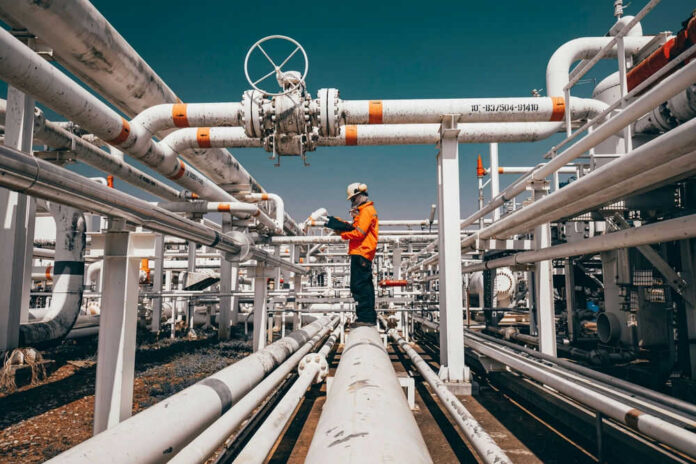 Worker in orange jacket inspecting industrial pipes.